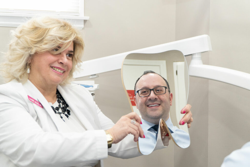doctor holding up mirror for patient to see dental procedure results and while smiling